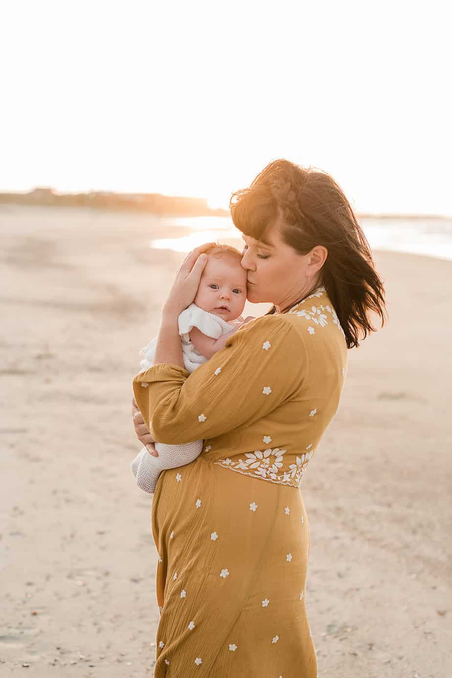 a mother at the beach kissing her newborns temple with destin florida family photographers Andrea Krey
