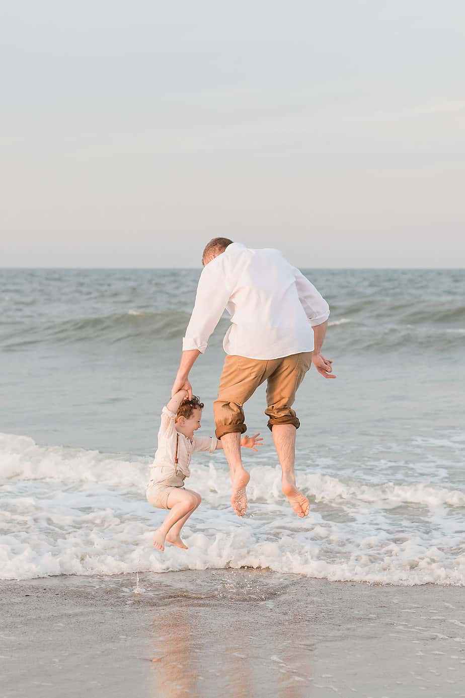 a father and son jumping by the ocean