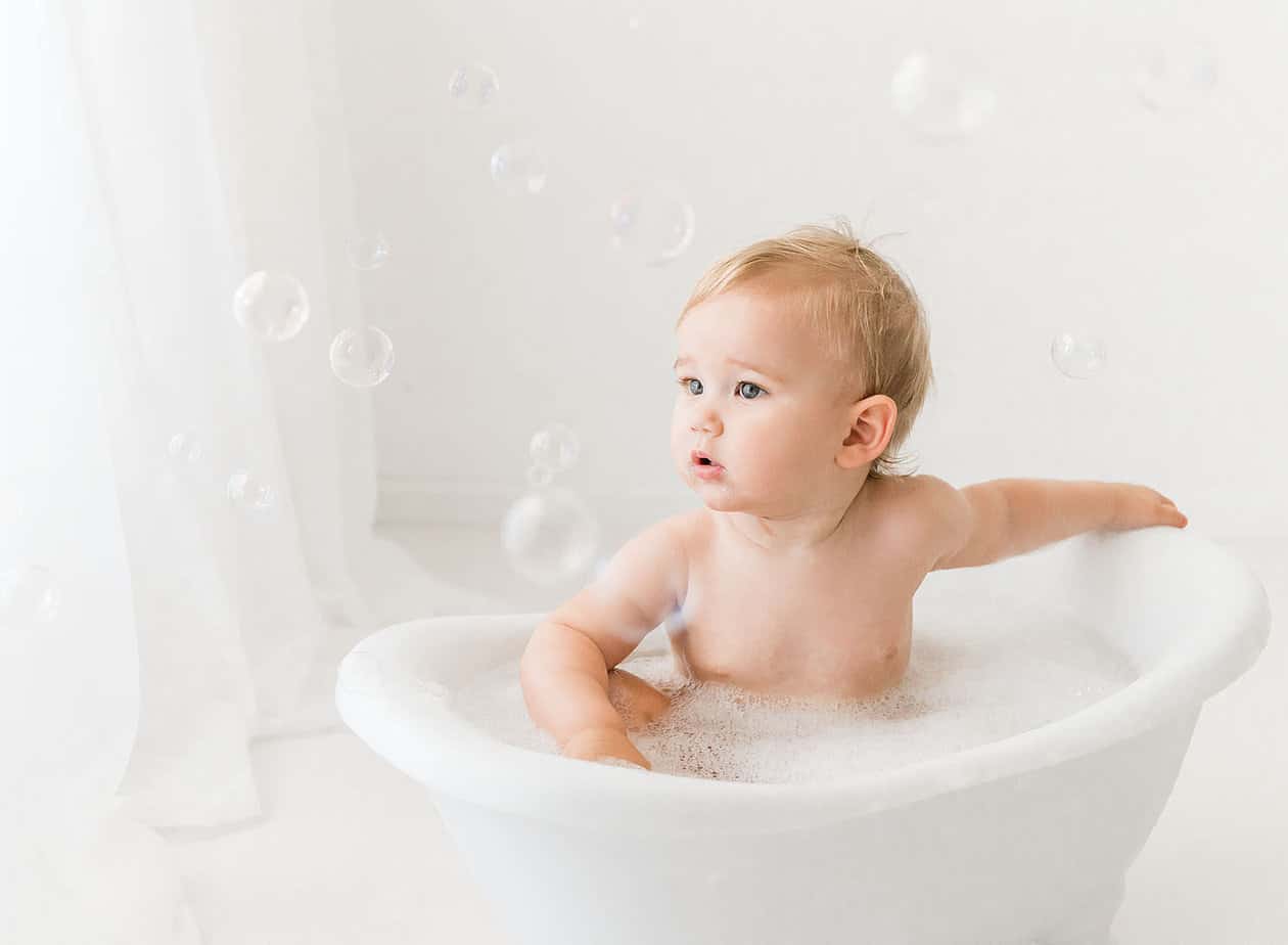 little boy in white bathtub after eating his smash cake
