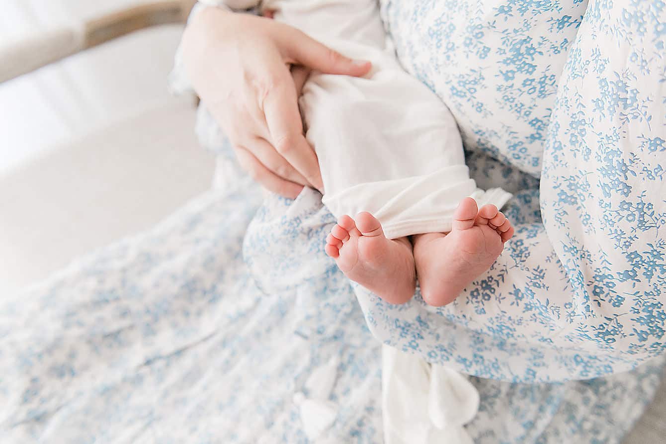 A person in a blue floral outfit holds a baby wrapped in white fabric, showing only the baby's feet. Captured by a talented Niceville photographer, this tender moment beautifully showcases the art of newborn photography.