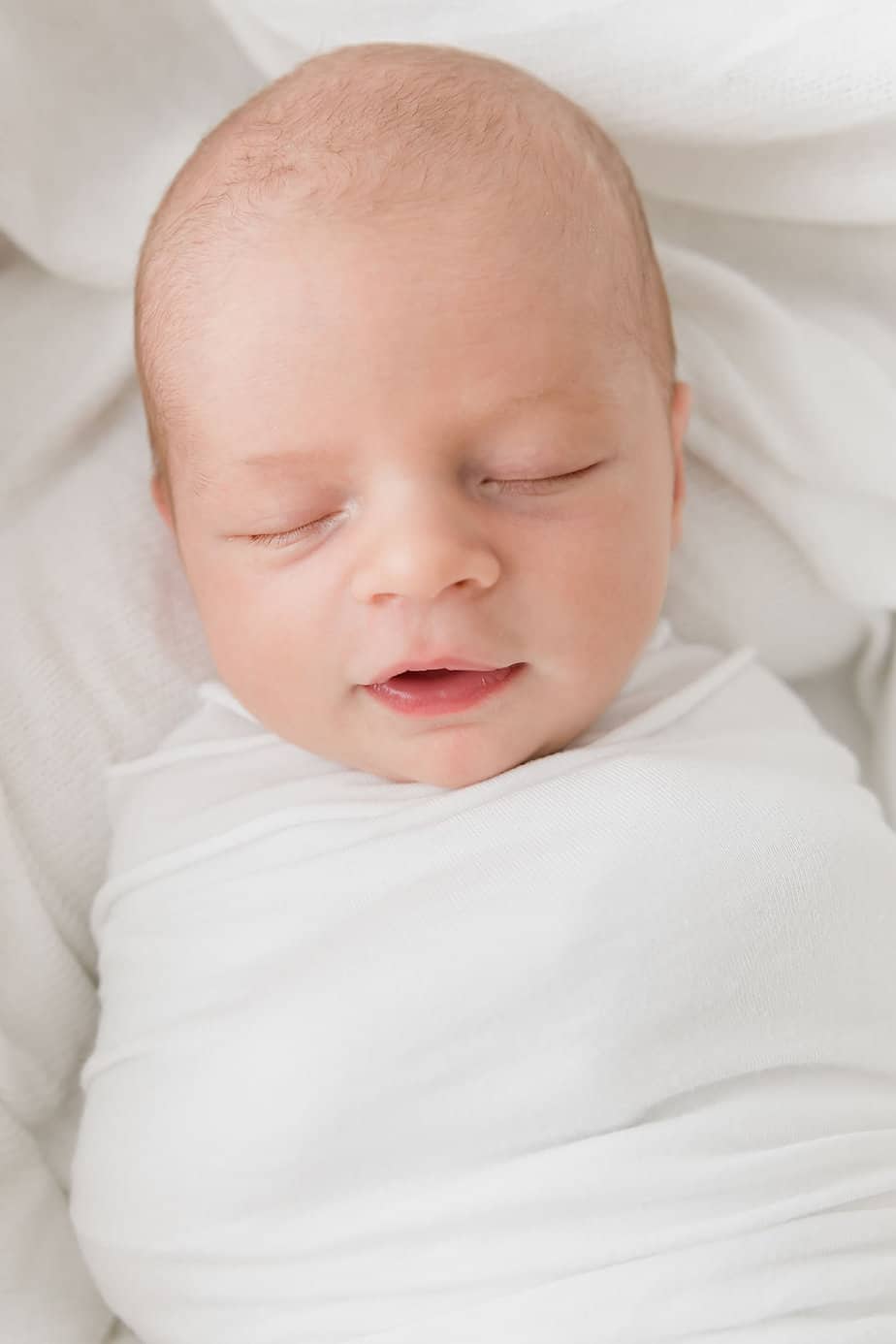 A sleeping newborn baby swaddled in a white blanket.