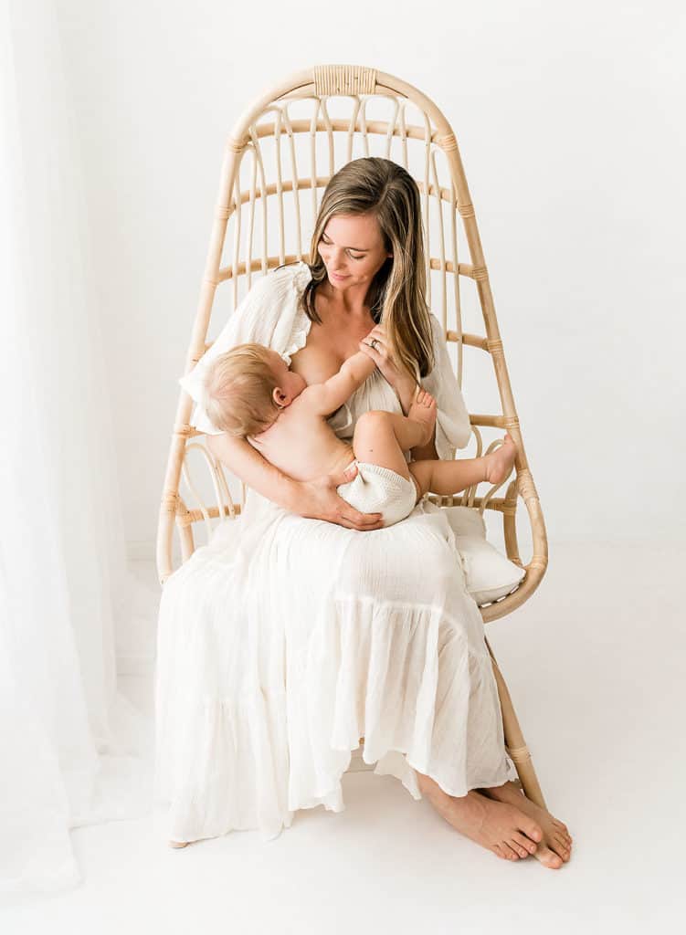 A woman is nourishing her baby in a rattan chair.