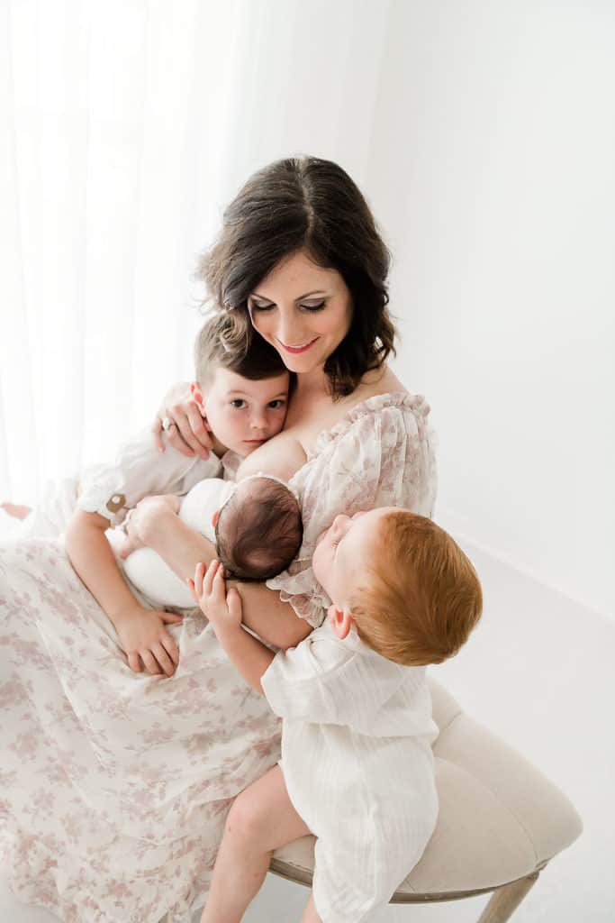 A woman is holding her two sons and a baby in front of a white background, showcasing the importance of family nutrition.