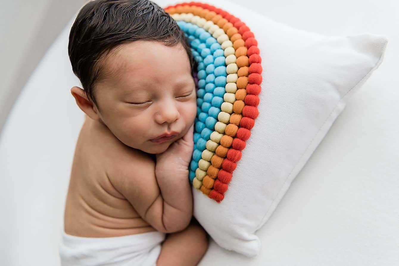 A baby sleeping on a pillow with a rainbow on it.