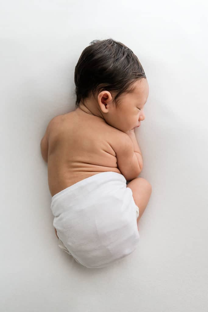 a newborn all curled up on a white blanket