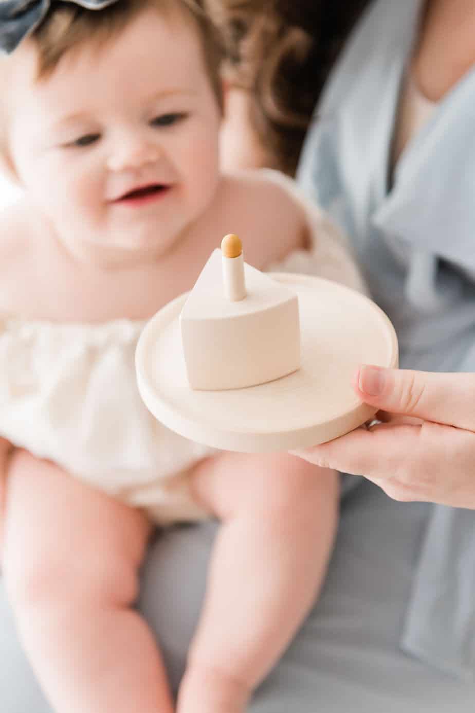 mother holding up a wooden cake with one candle while her daughter smiles down on it
