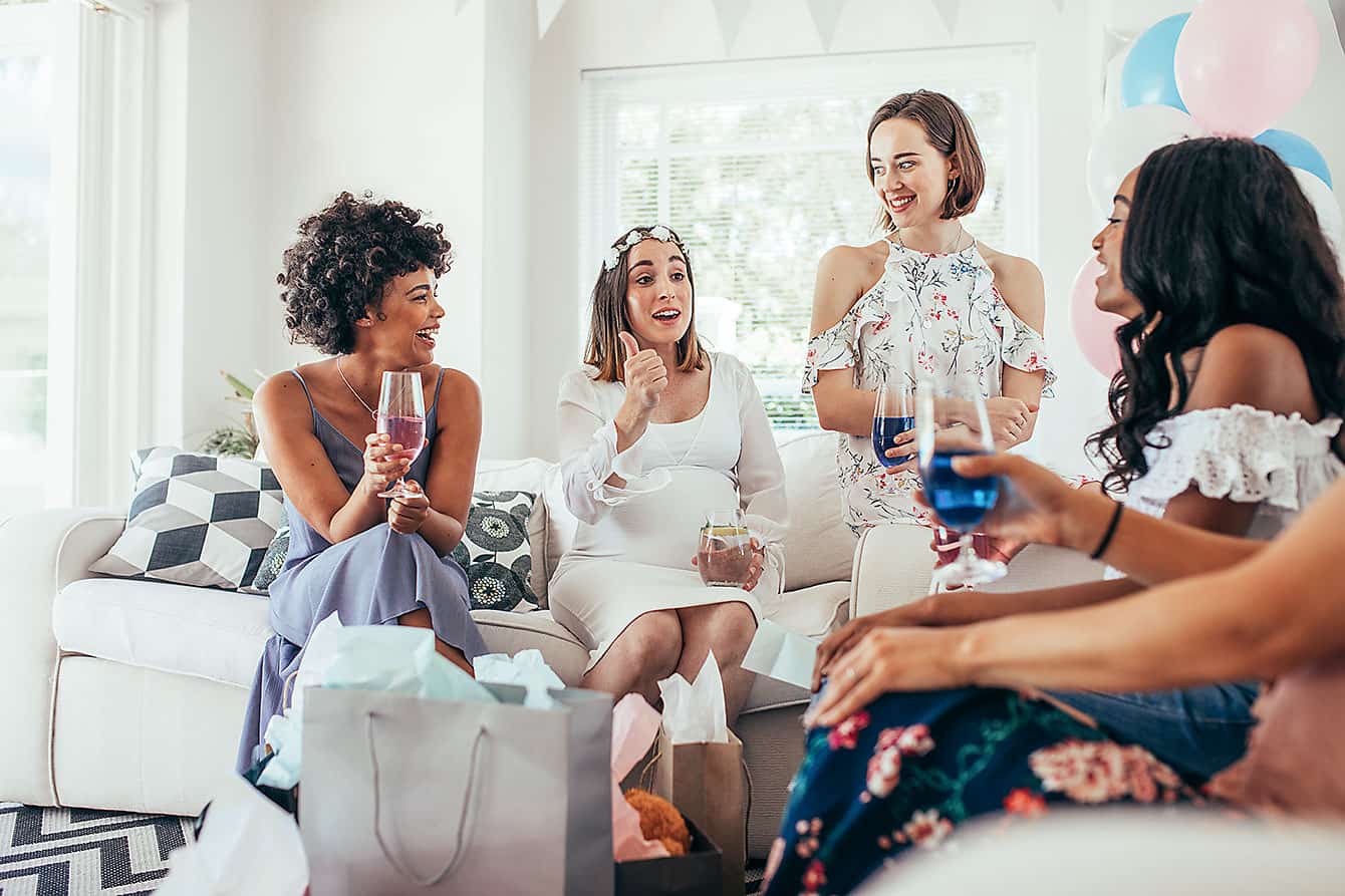 Four women relax on a couch at a baby shower, chatting and sipping drinks at one of the top baby shower venues in Pensacola FL.