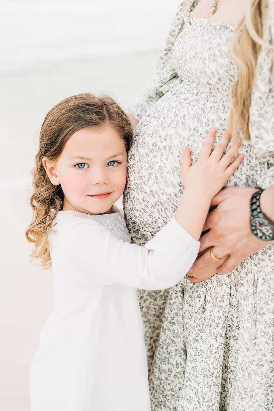 a little girl holding her moms pregnant belly