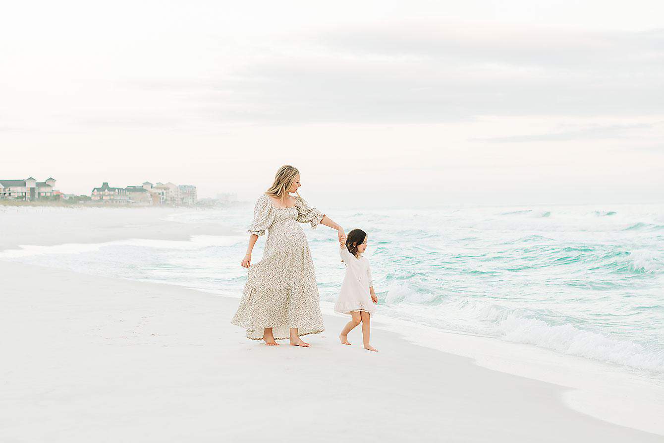 a pregnant woman and her little girl going for a walk at the beach
