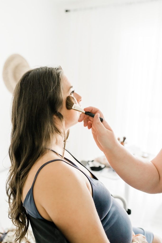 Pregnant woman getting professional makeup done by a makeup artist in Destin FL before her maternity session