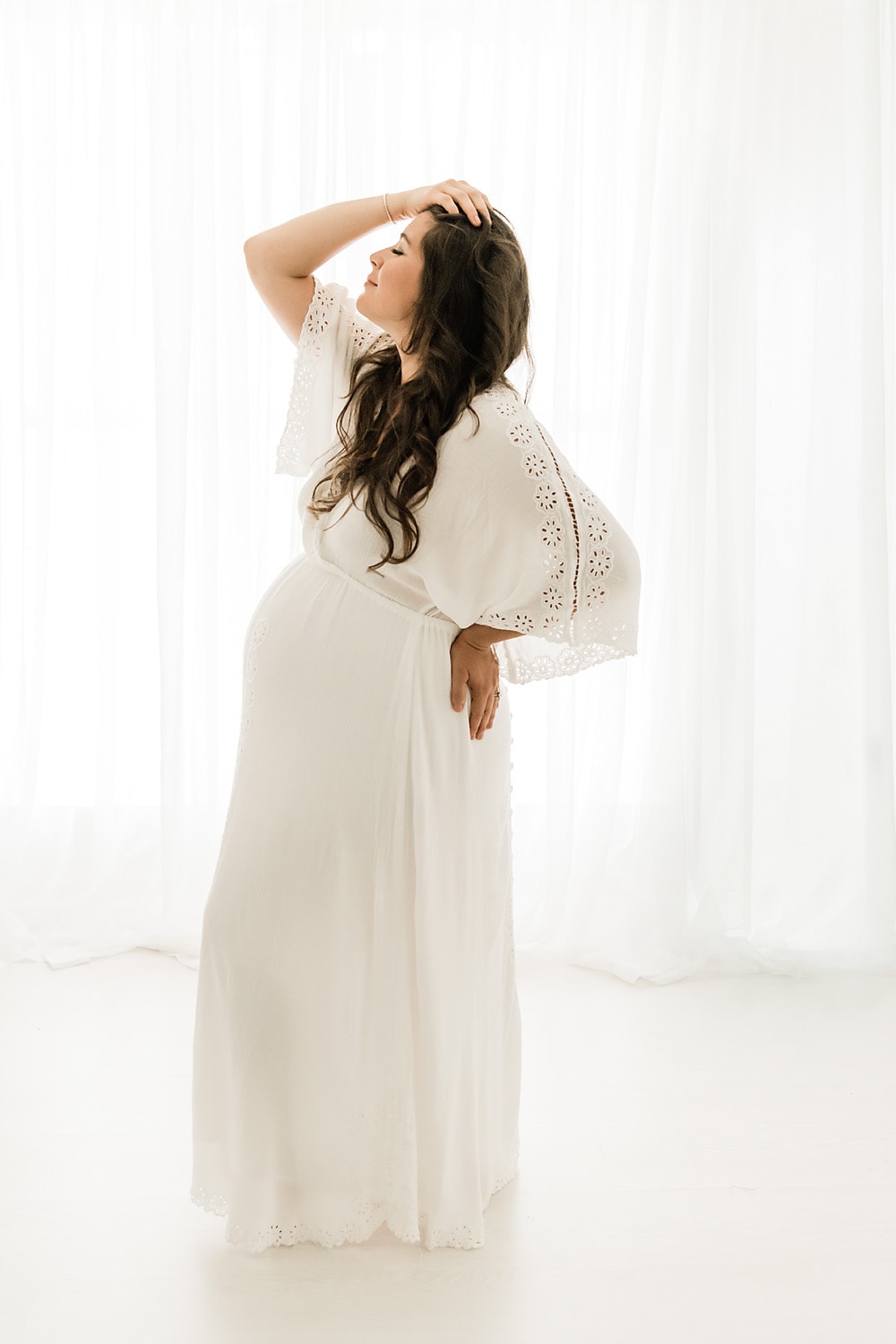 pregnant woman posing in front of a white window