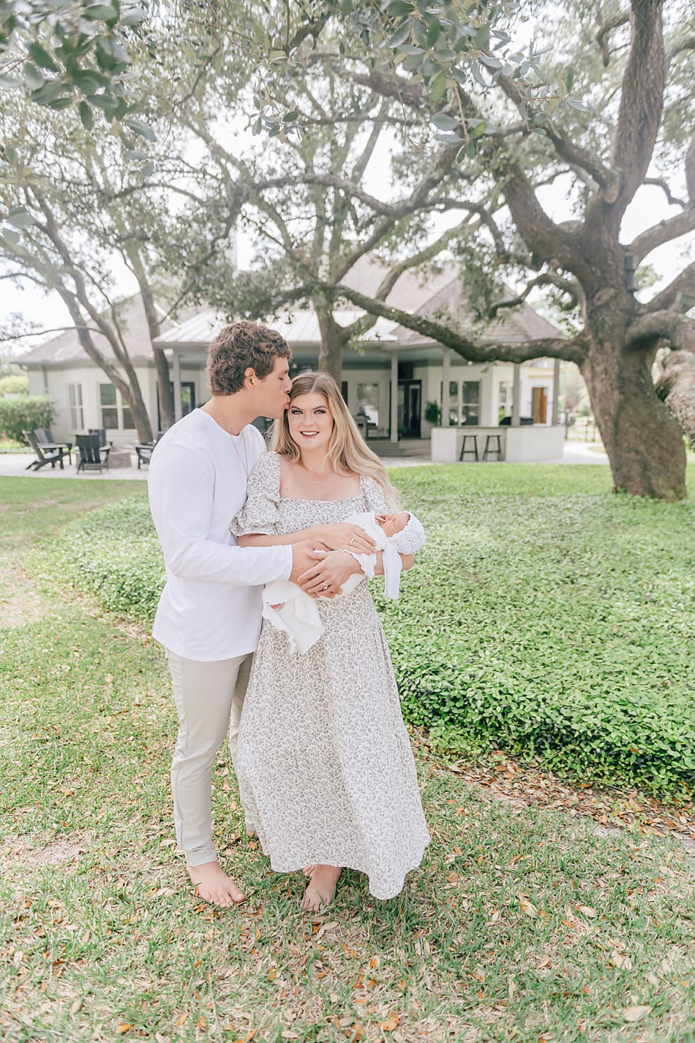 a young couple holding their new baby in front of their house by Mobile newborn photographer