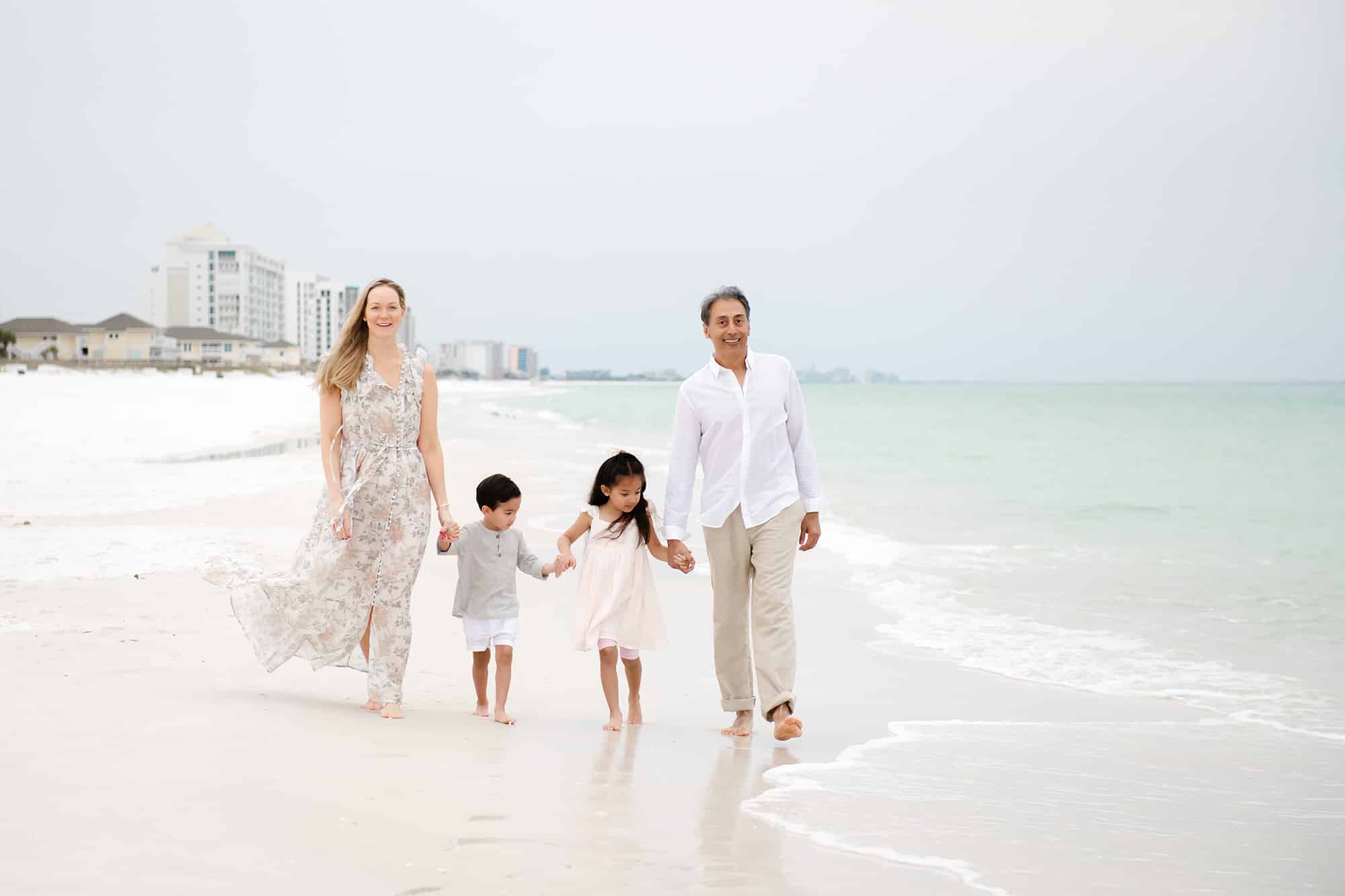 Four people, two adults and two kids, stroll barefoot on a cloudy beach&mdash;perfect family time in Pediatric Dentist Niceville style.