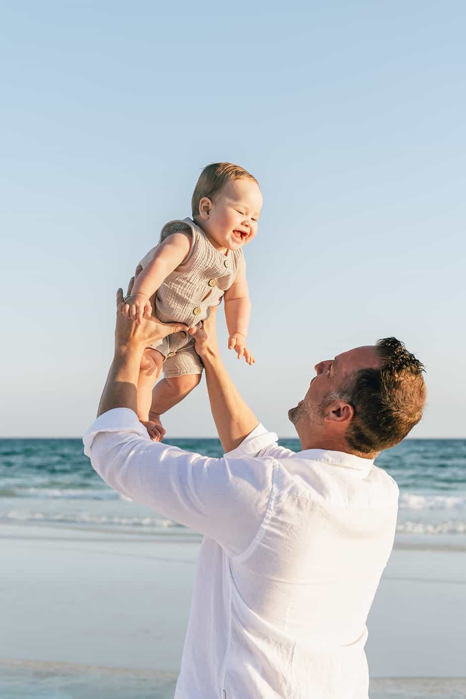 a father tossing his baby in the air at the beach