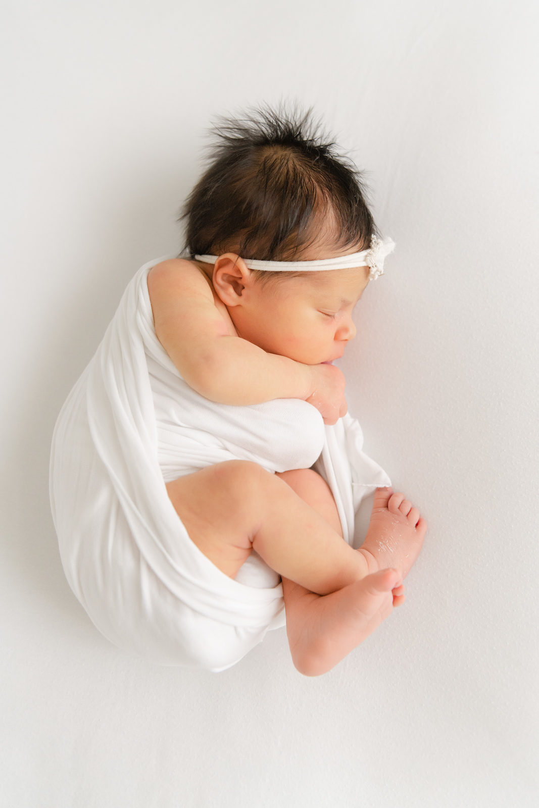 a newborn baby curled up on a white blanket