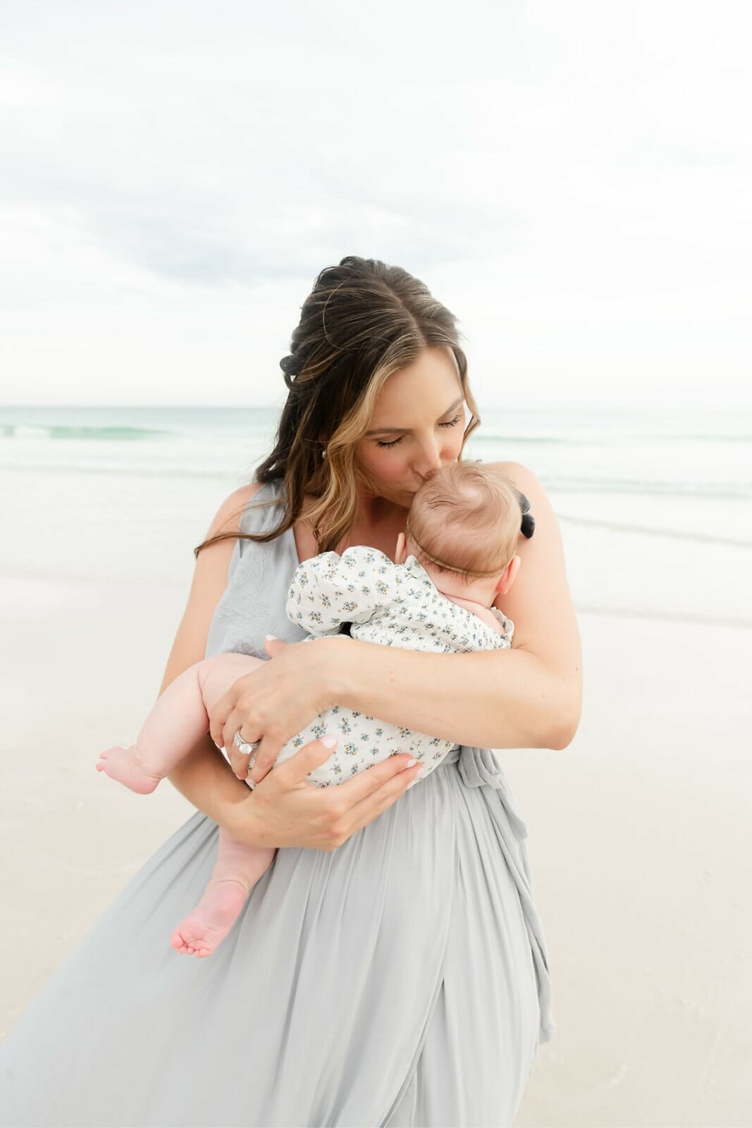 A woman in a gray dress holding a baby on the beach Destin Holiday Isle.