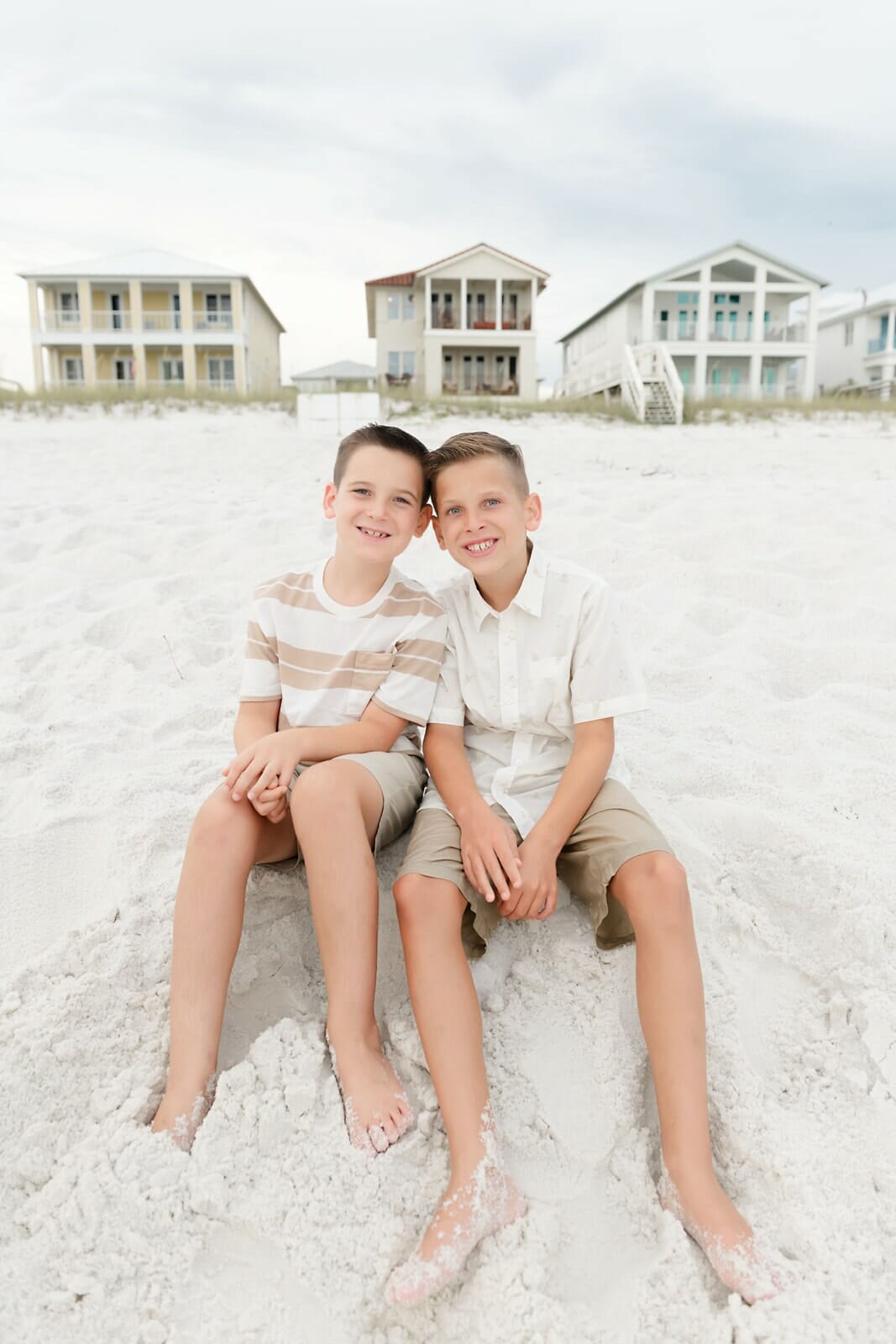 Two boys sitting on the beach in front of houses Destin Holiday Isle.