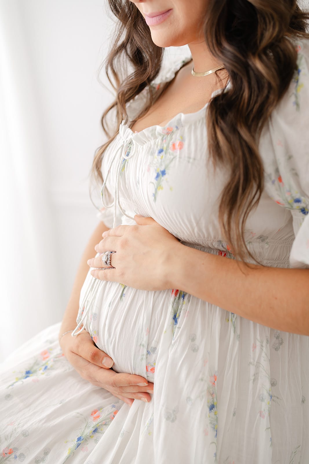 A Pensacola maternity photographer captures a serene moment as a pregnant woman in a white dress lovingly cradles her belly.
