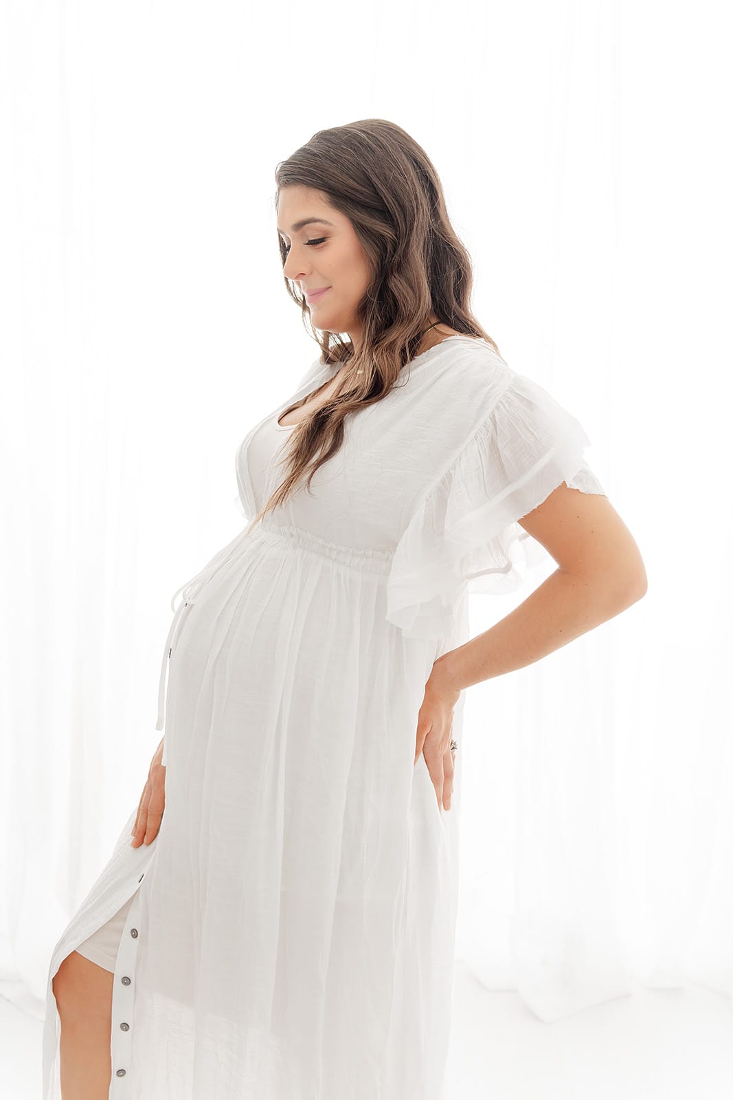 A Pensacola maternity photographer captures a radiant pregnant woman in a white maternity dress.