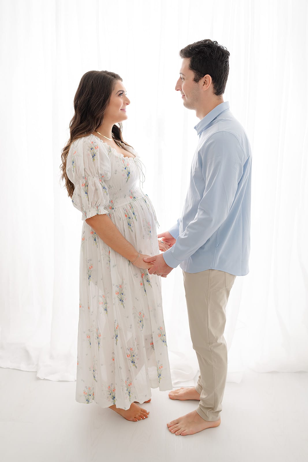 a pregnant couple standing in front of a white backdrop.