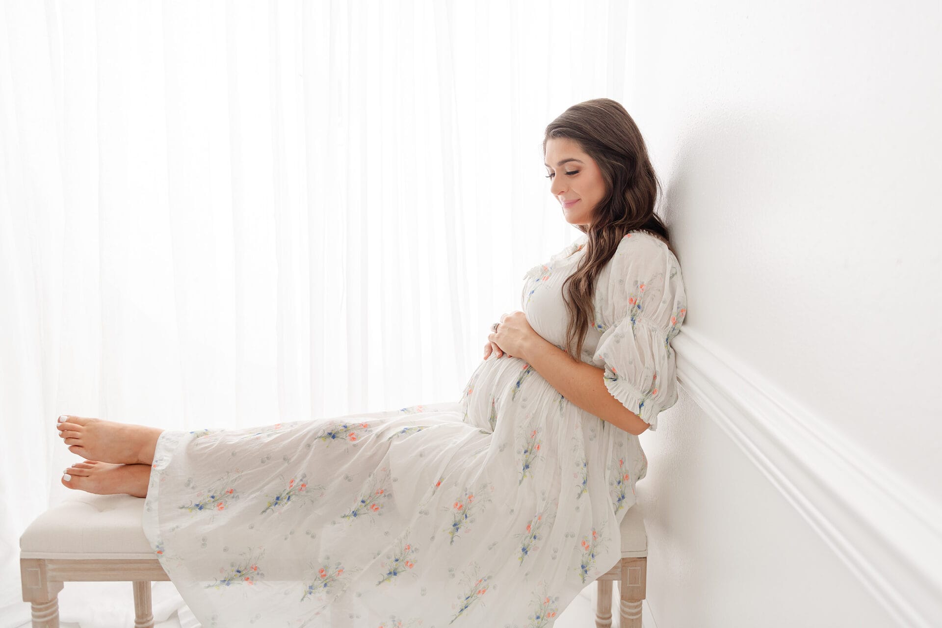 Pregnant woman sitting on a bench in a white room.