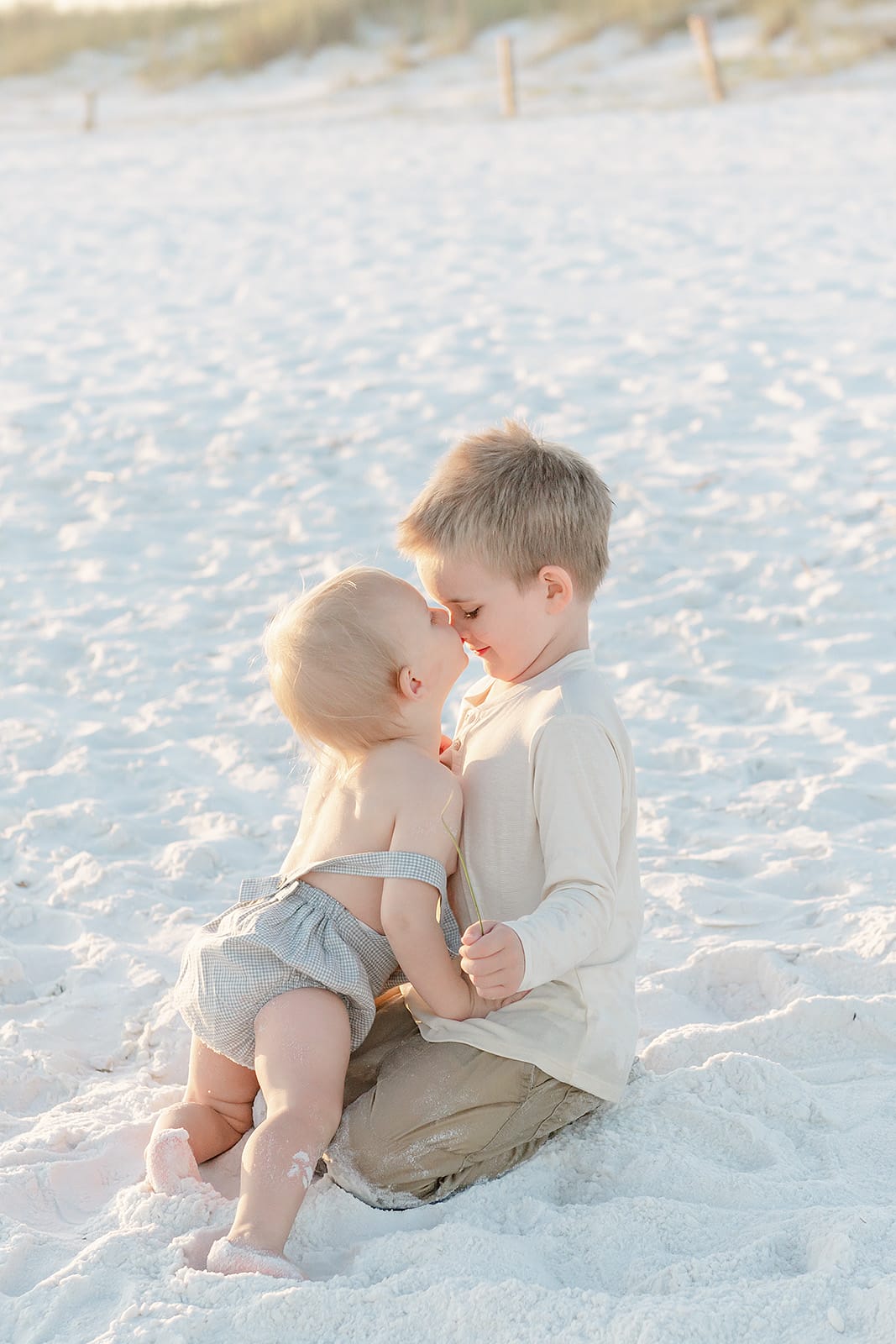 Two children kissing in the sand on the beach.