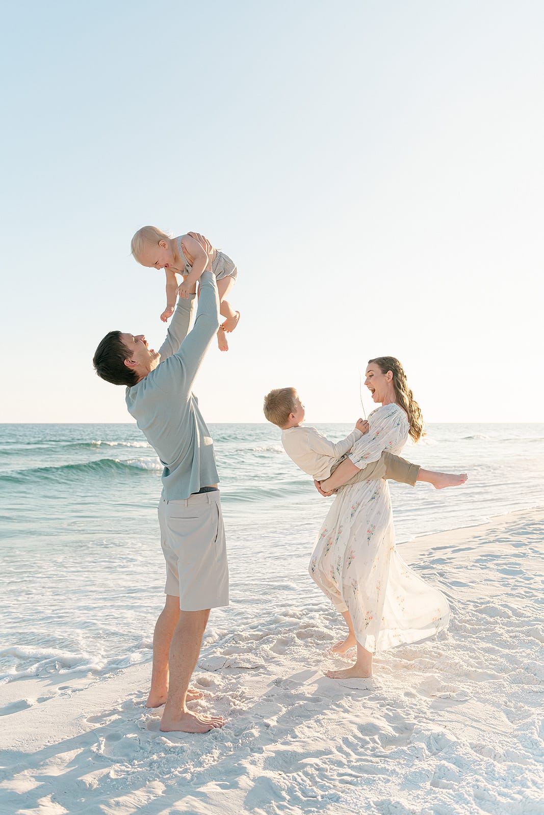 A family is playing on the beach with a baby in the air.