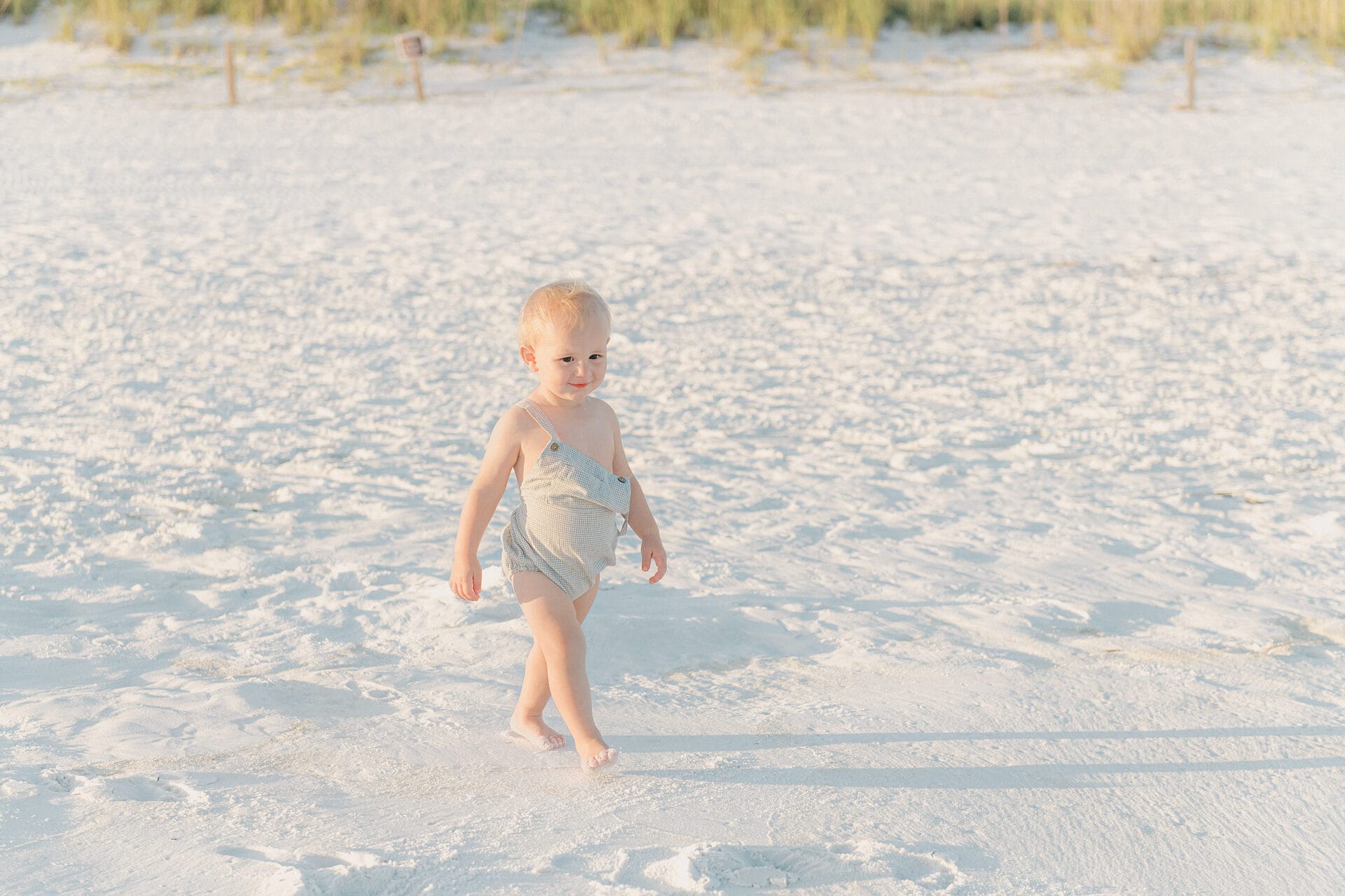 A baby walking in the sand on the beach.