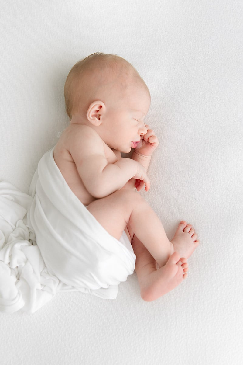 Sleeping newborn baby wrapped in white, captured in soft natural light at a Niceville FL newborn photography studio
