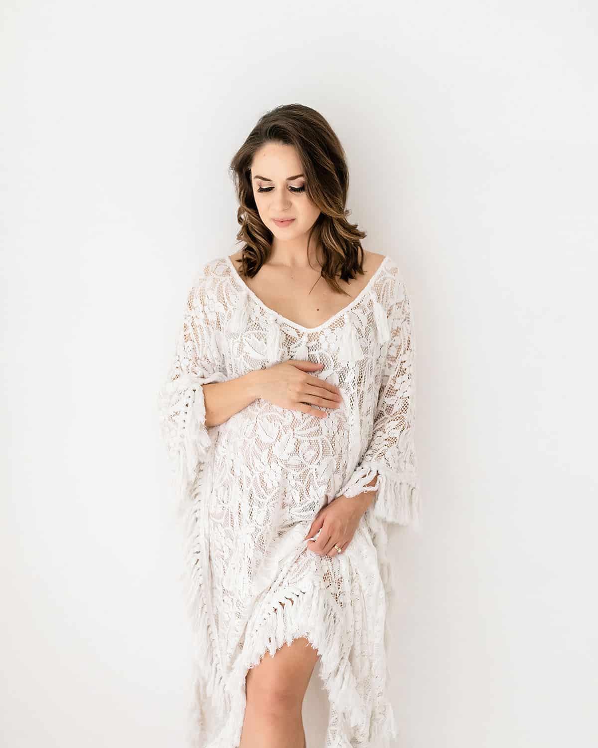 studio-maternity-session-white-lace-fringe-kimono-portrait.jpg Alt text: Expecting mother in a white lace fringe kimono gently cradling her bump during an intimate studio maternity portrait session