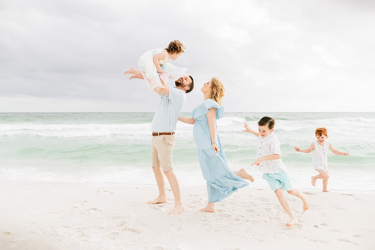 Dad tossing his daughter in the air while the family laughs and plays on the beach in Destin