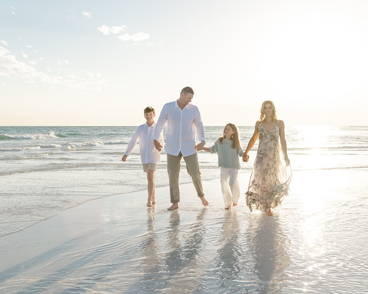 Family of four walking hand in hand along the shoreline at Henderson Beach State Park in Destin