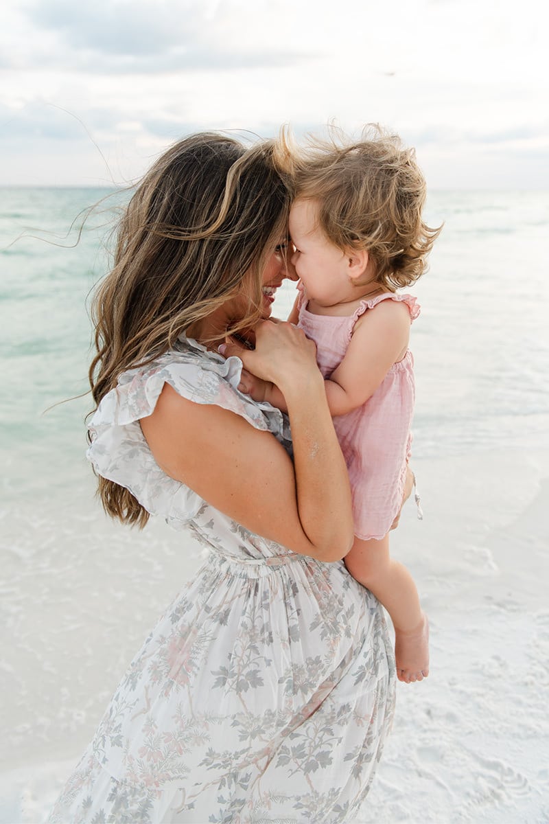 Mother holding her toddler nose to nose at the water's edge during a beach session in Destin