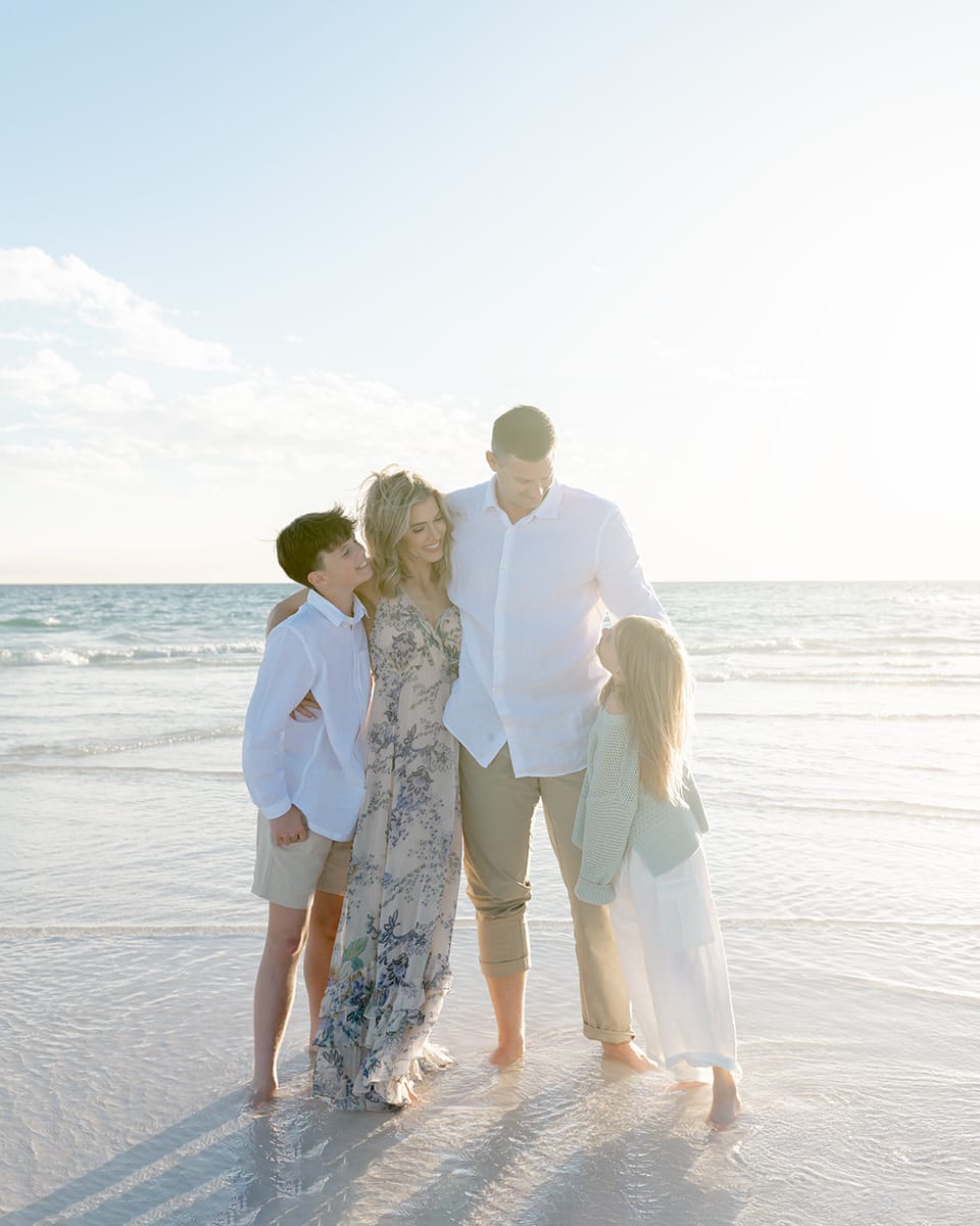 Family of four standing together in the surf at golden hour during a Destin family photography session