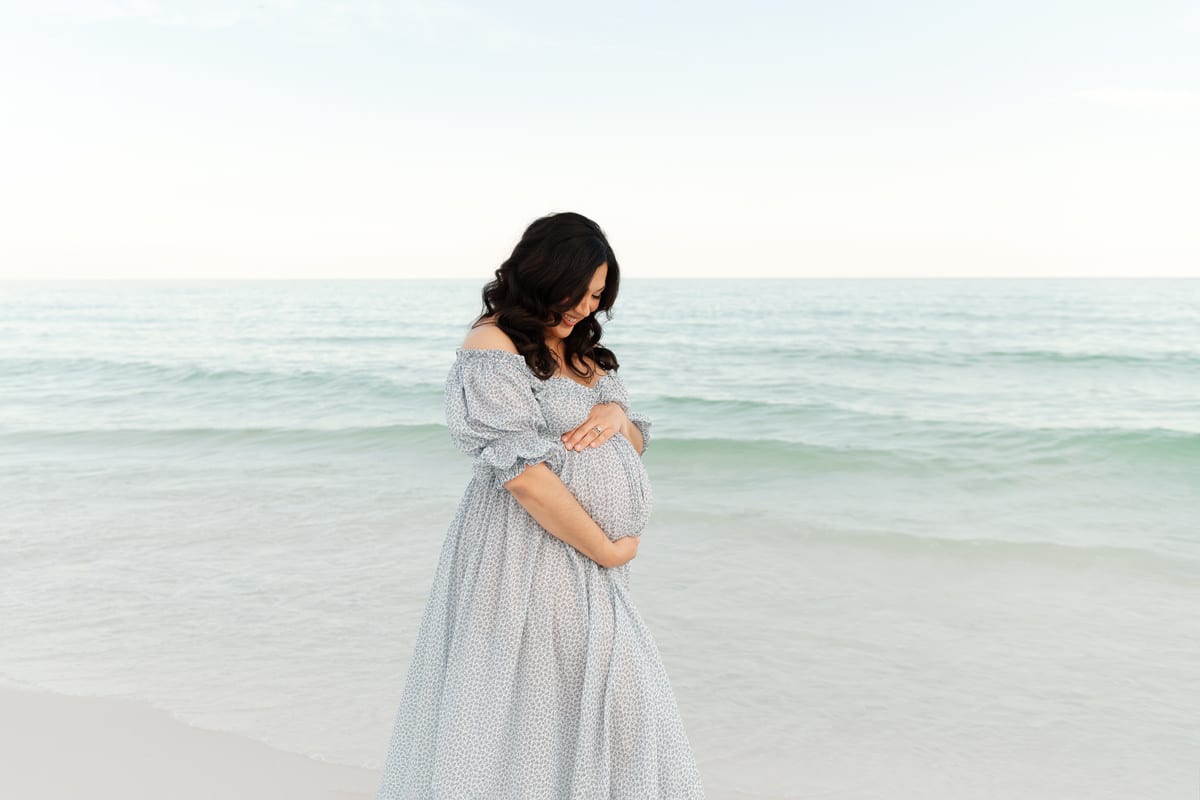 Expecting mama in a blue floral gown cradling her bump at a Destin beach maternity session