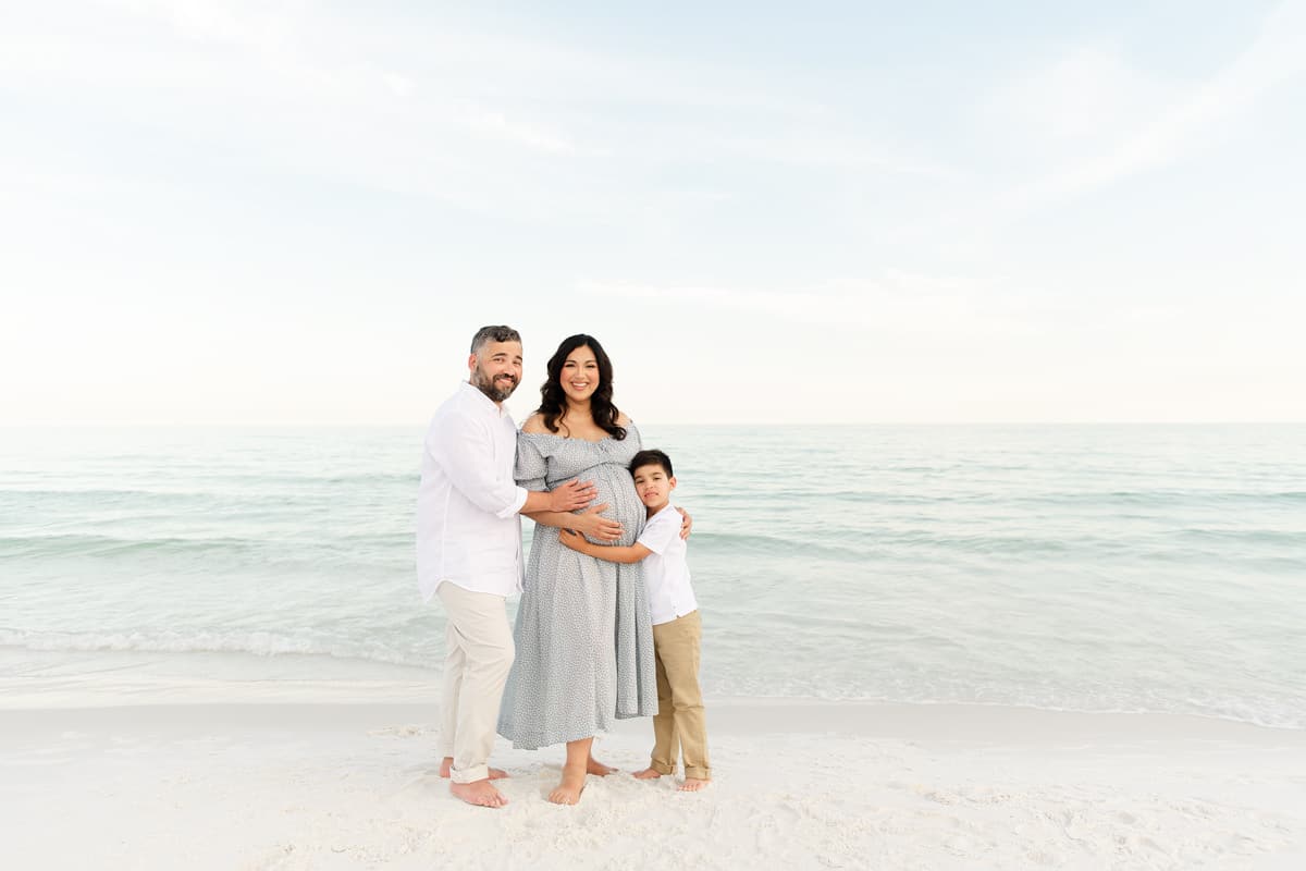 Family at a Destin beach maternity session, dad, big brother, and expecting mama at the water's edge