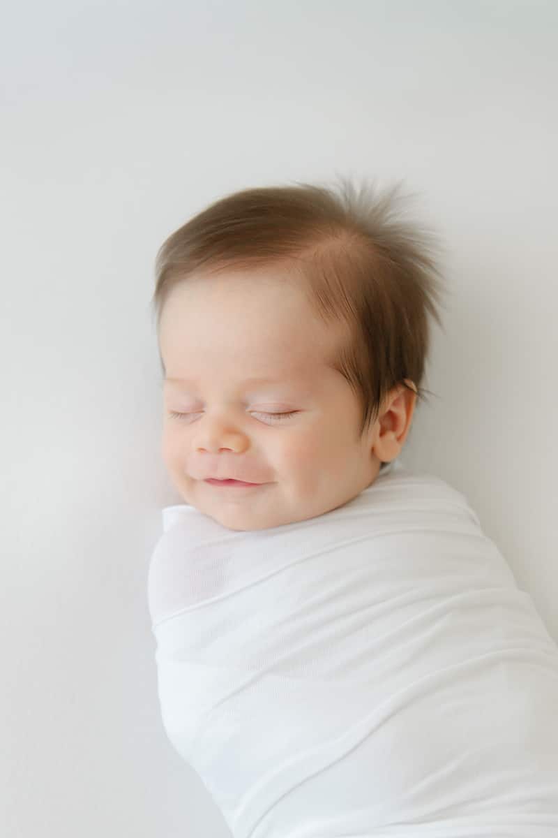Sleeping newborn smiling in a white swaddle captured by an Emerald Coast newborn photographer