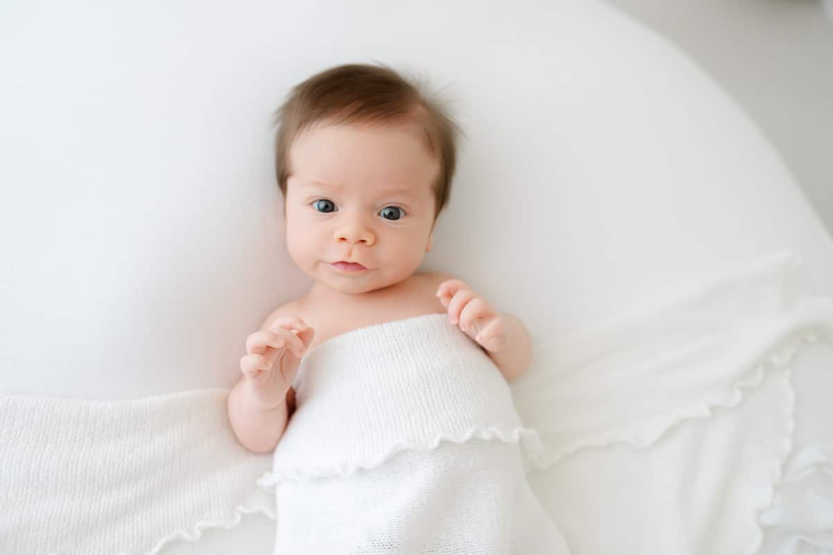 Newborn baby looking at camera with tiny hands raised photographed by an Emerald Coast newborn photographer