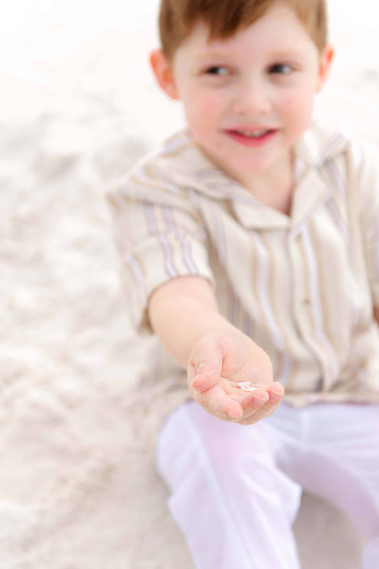 Little boy holding out his sandy hands toward the camera on a Destin beach, photographed by a Miramar Beach photographer