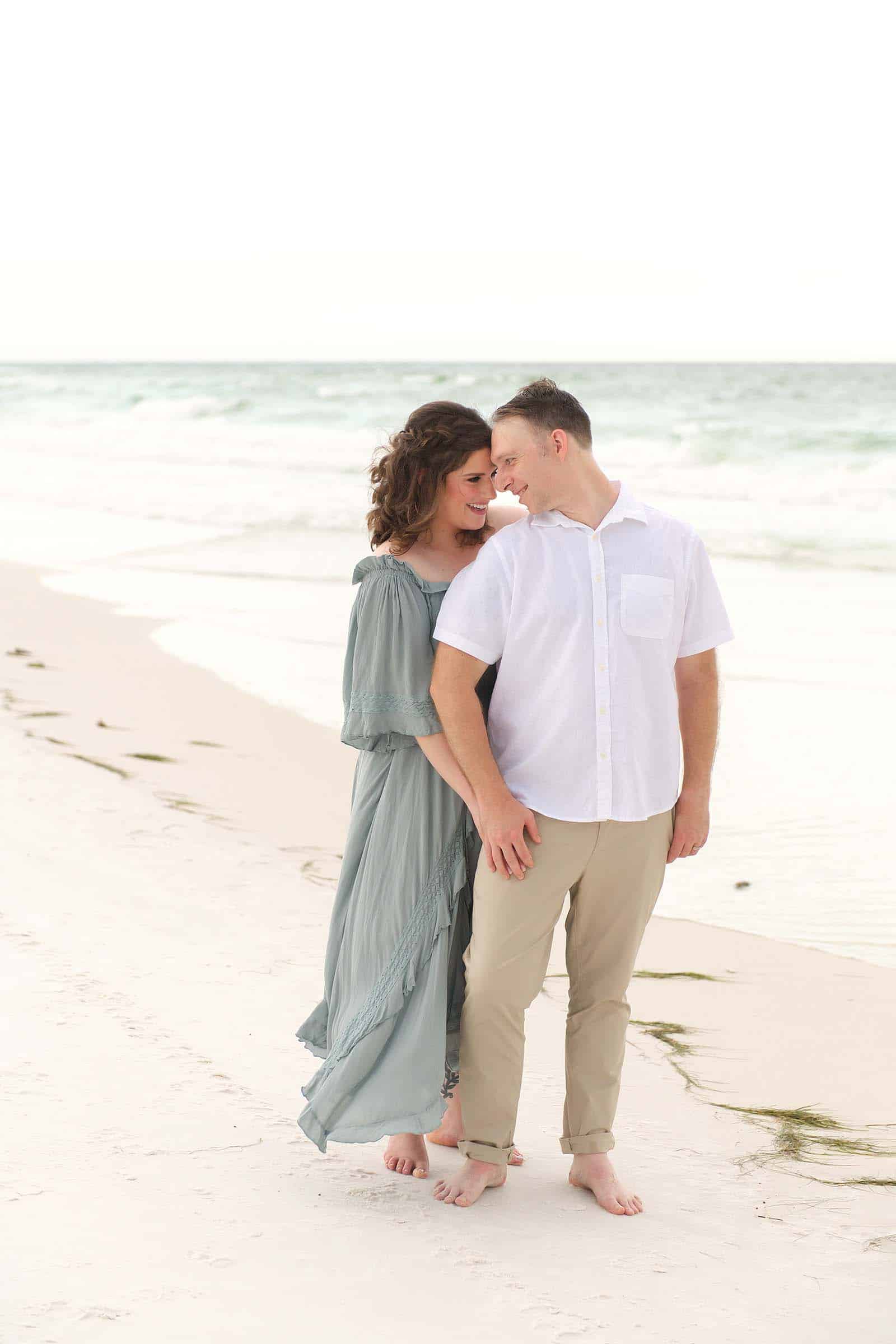 Couple standing close together on a Destin beach, foreheads nearly touching, photographed by photographers in Miramar Beach Florida