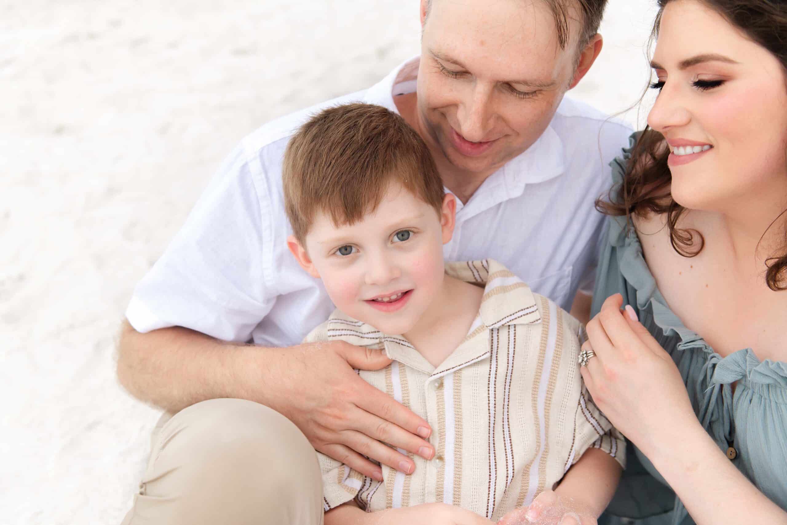Close-up portrait of a little boy looking at the camera with his parents beside him, captured by a Miramar Beach family photographer