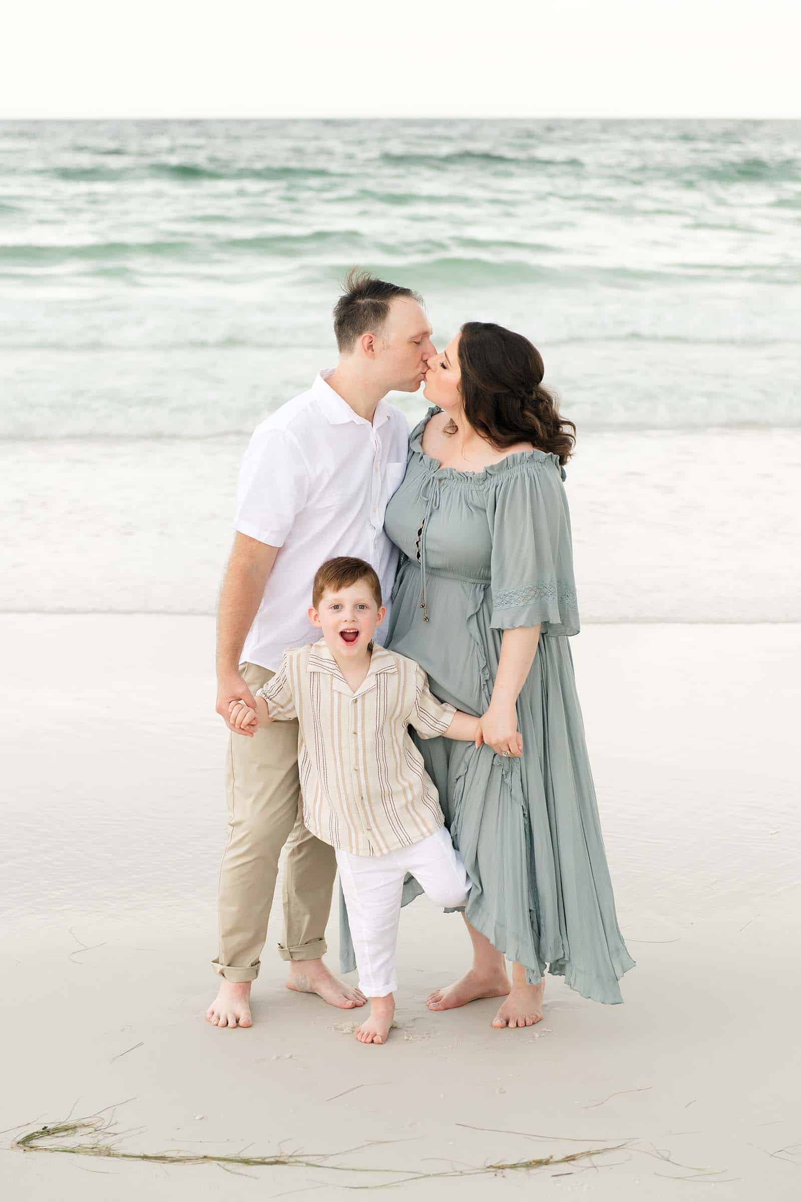 Parents sharing a kiss on a Destin beach while their little boy makes a funny face between them, captured by photographers in Miramar Beach Florida