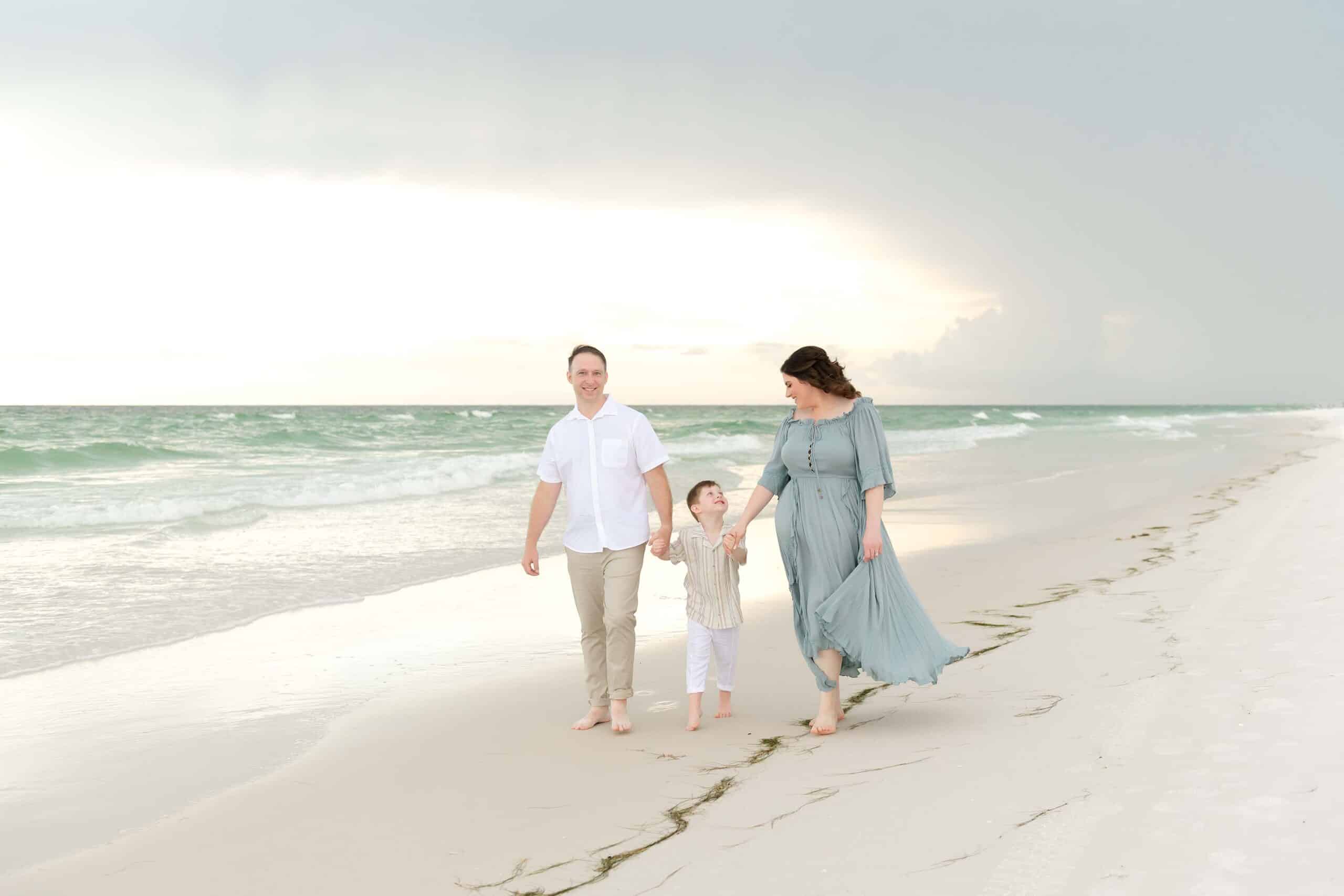 Family of three walking hand in hand along the shoreline, little boy looking up at his mom, photographed by a Miramar Beach family photographer