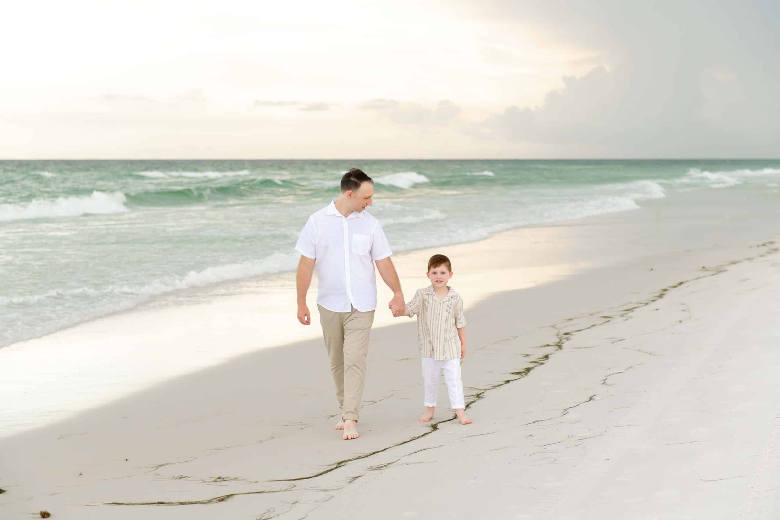 Father and son walking hand in hand along the shoreline on a Destin beach, photographed by a Miramar Beach photographer