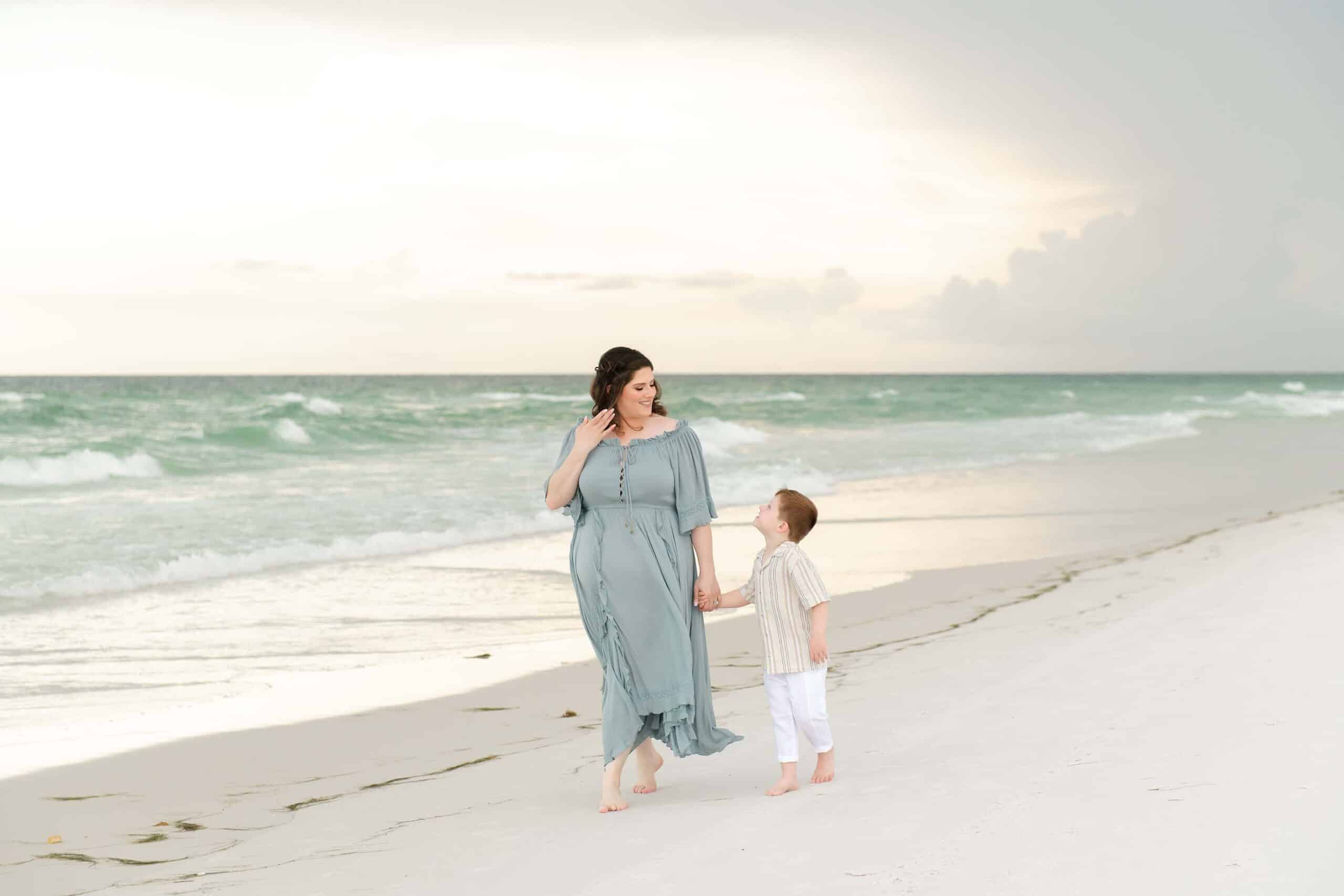Mother and son walking together on a Destin beach, her little boy looking up at her with love, captured by photographers in Miramar Beach Florida