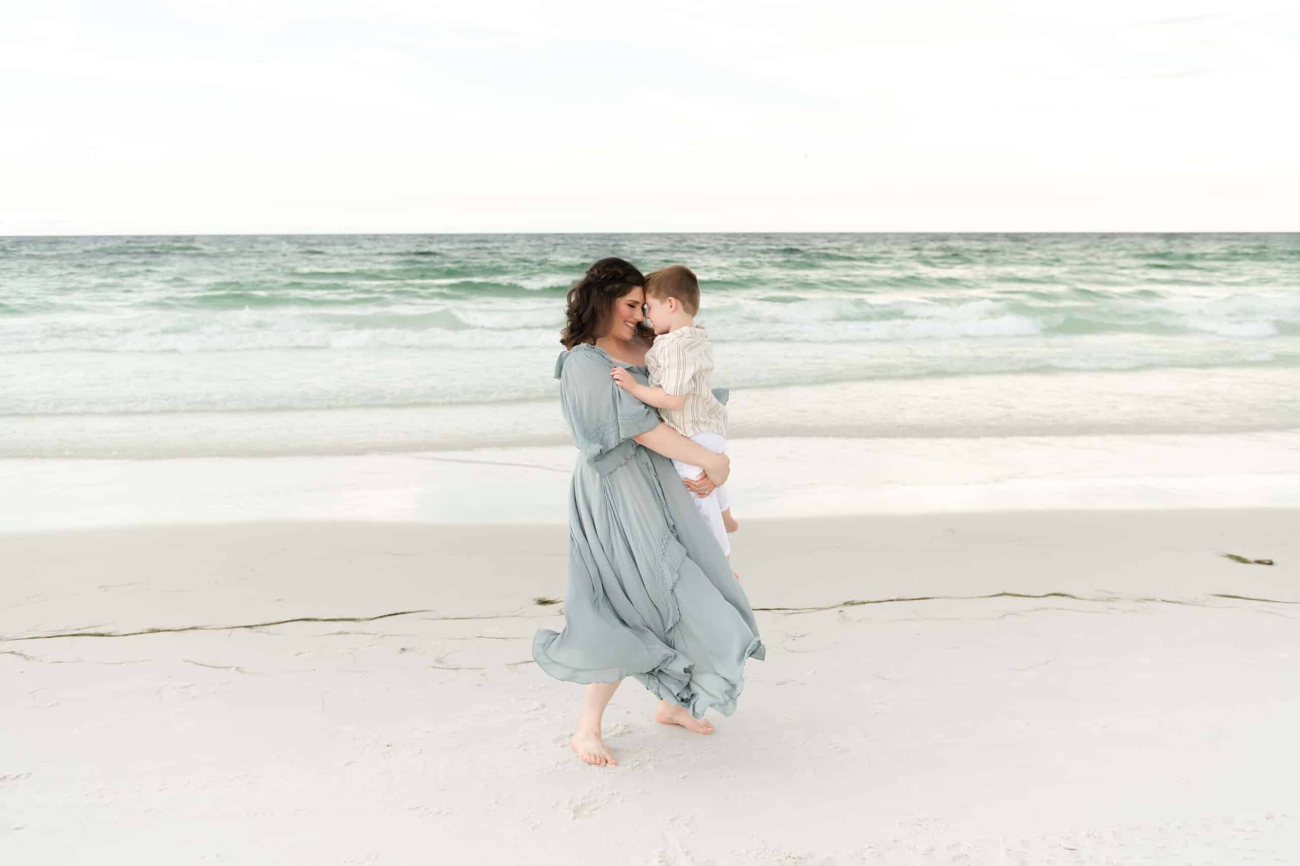 Mother holding her son close on a Destin beach, foreheads touching and smiling at each other, photographed by a Miramar Beach family photographer