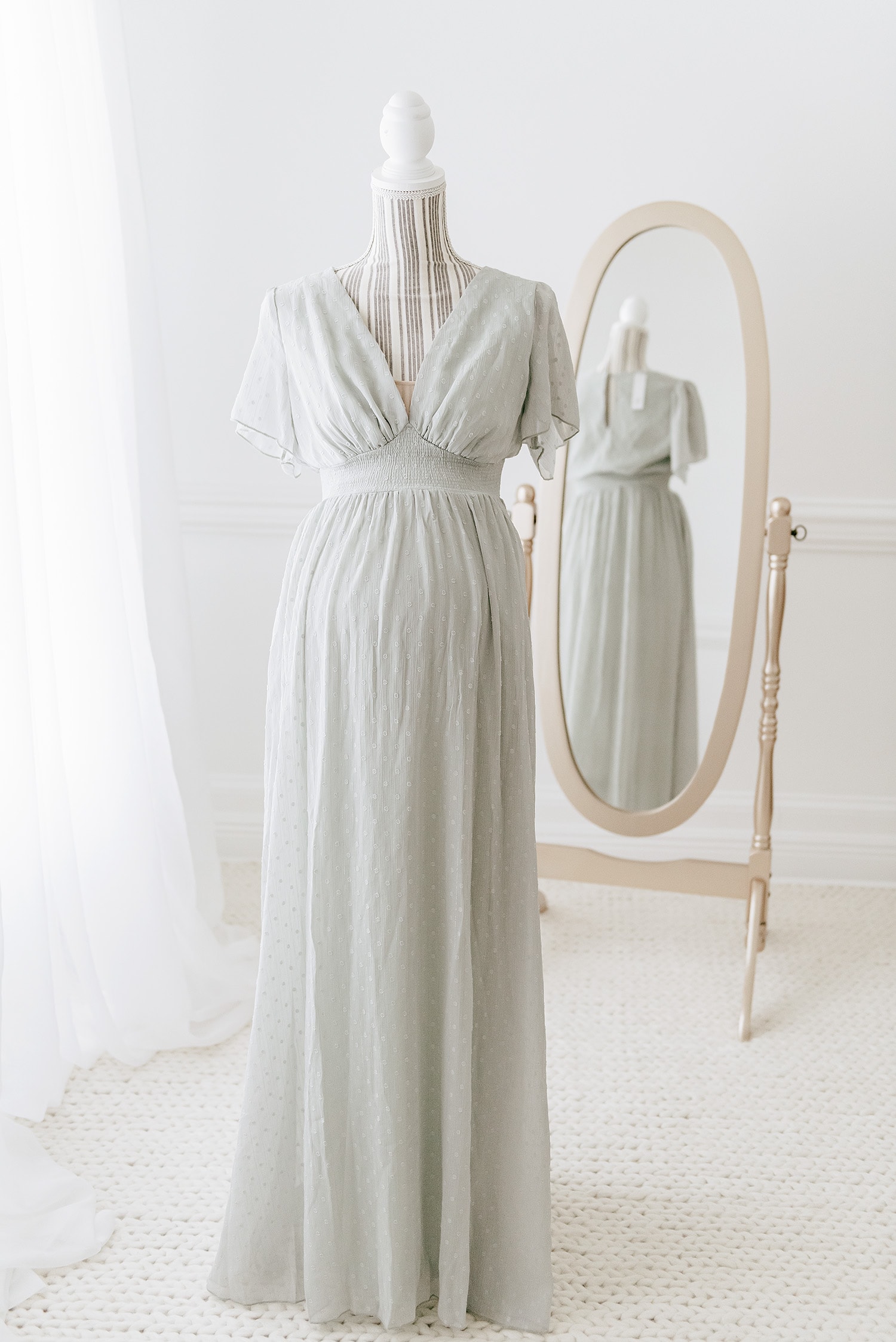 Sage green flowing maternity gown with flutter sleeves and smocked waistline on dress form, demonstrating bump-friendly silhouette for what to wear maternity photos Destin beach