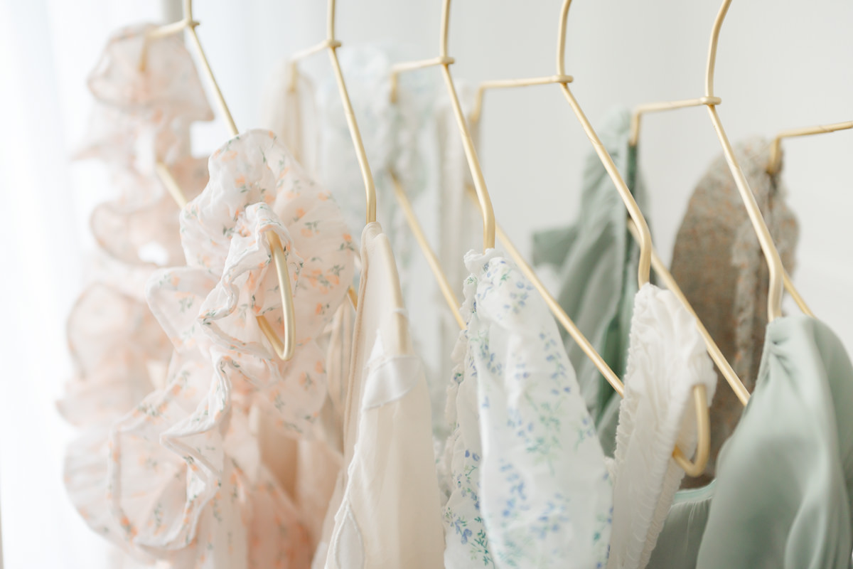 Close-up of blush, sage, and blue floral dresses on gold hangers in my client closet