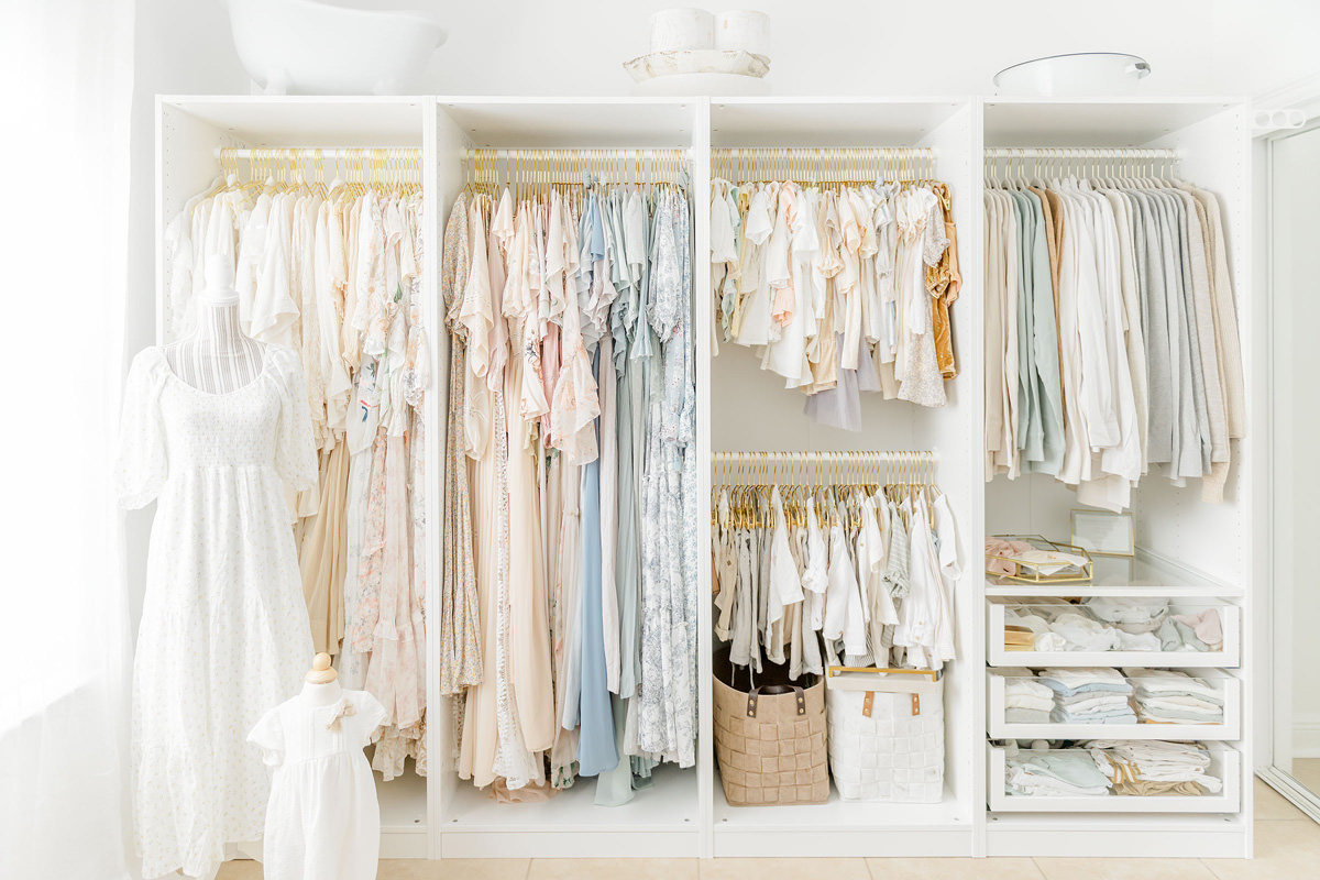 My client closet with neutral and soft pastel dresses, shirts, and children's pieces on white shelves in my Niceville studio