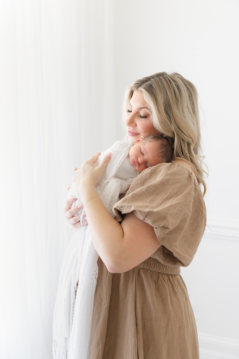 A woman in a tan dress holding a newborn baby, captured by a Shalimar newborn photographer.